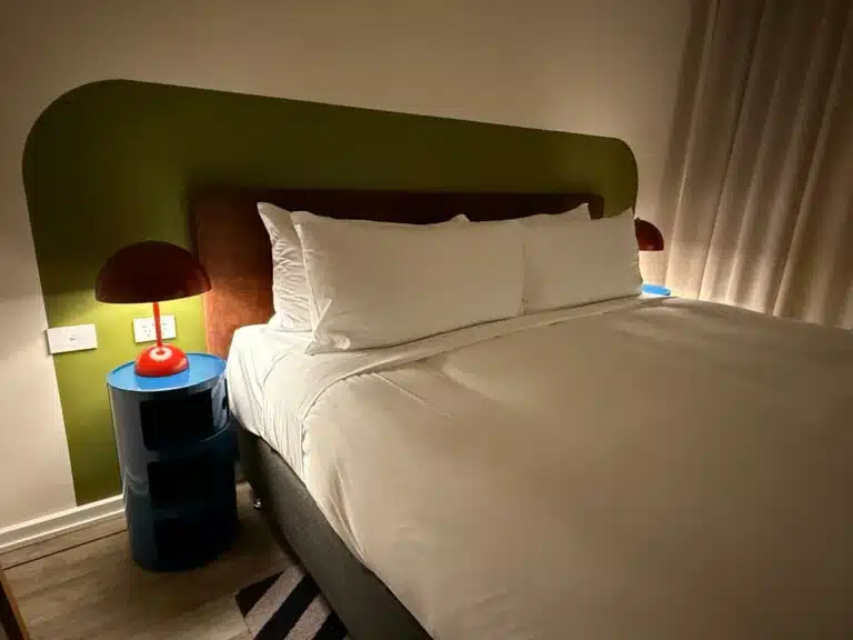 A Bed With White Sheets And A Red Lamp